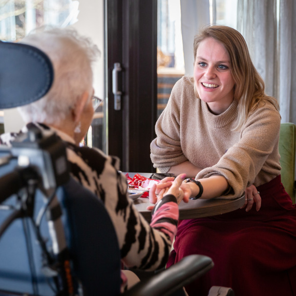 Activiteiten Anna Ouderenzorg kalender Activiteitenbegeleider zit voor mevrouw in rolstoel en houdt haar hand vast